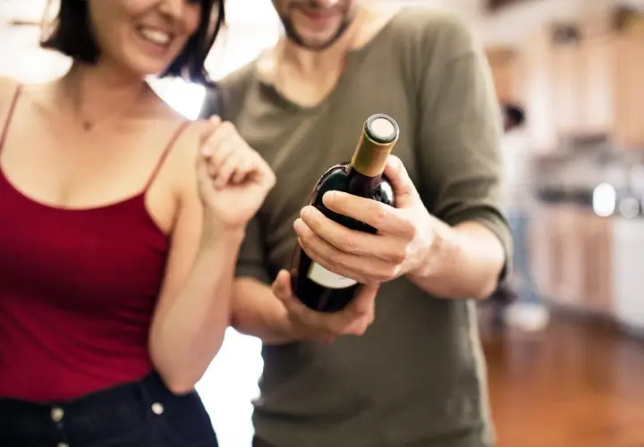 Un couple souriant admire une bouteille de vin rouge, prêt à partager un moment spécial.