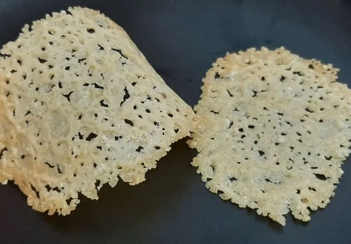 Deux tuiles de parmesan croustillantes et ajourées, posées sur une surface sombre.