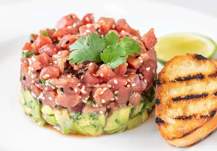 Délicieux tartare de bar frais, garni de sésame et de coriandre, servi avec des toasts grillés et une tranche de citron vert.