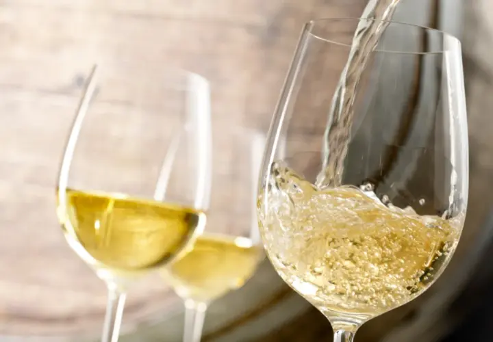 Le vin blanc est versé dans un verre, rappelant le processus de vinification. Deux autres verres sont visibles en arrière-plan.