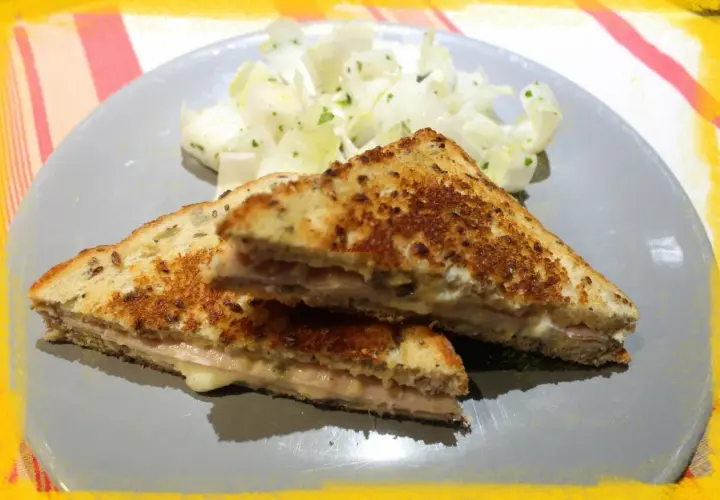 Un délicieux croque monsieur à la poêle, doré et garni de jambon et fromage fondant, servi avec une salade fraîche.
