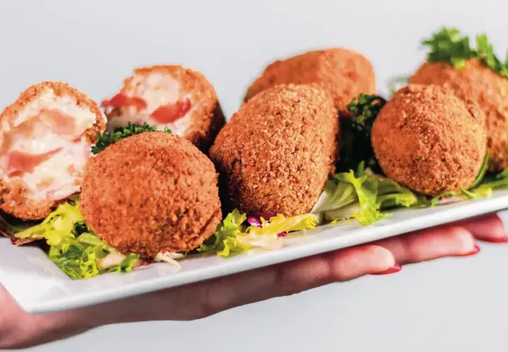 Assiette de croquetas de jambon dorées et croustillantes, garnie de salade verte.