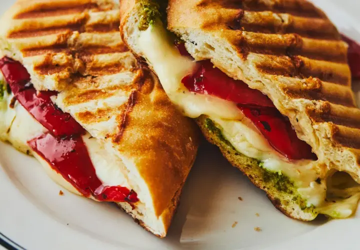 Un délicieux sandwich italien grillé, garni de fromage fondant, de poivrons rouges et de pesto vert.