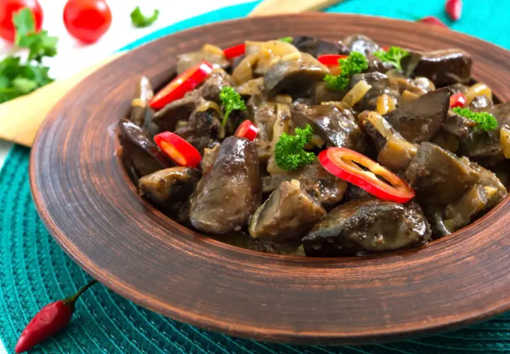 Un plat appétissant de foie de volaille mijoté avec des oignons et garni de persil frais et de rondelles de piment rouge.