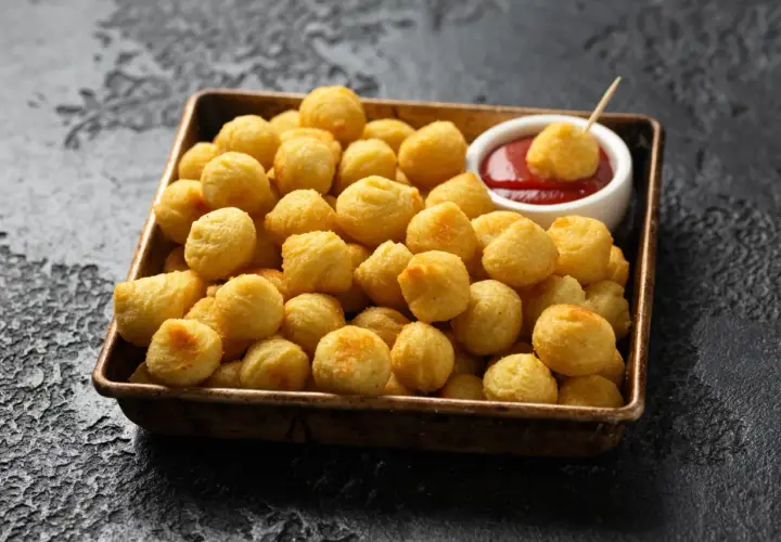 Un plateau rempli de pommes dauphine dorées et croustillantes, prêtes à être trempées dans une sauce tomate.