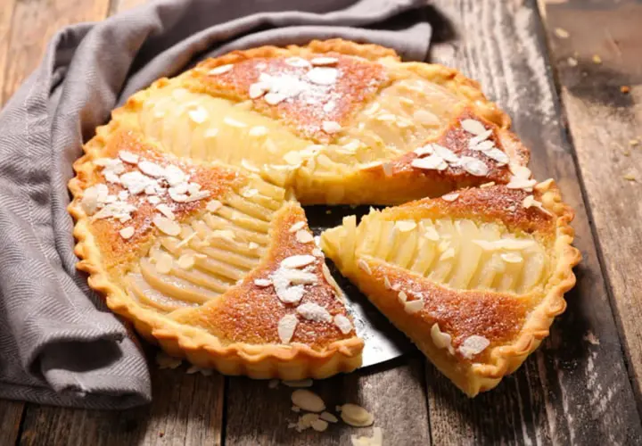 Une délicieuse tarte au poire, garnie d'amandes effilées et saupoudrée de sucre glace, repose sur un plateau en bois.
