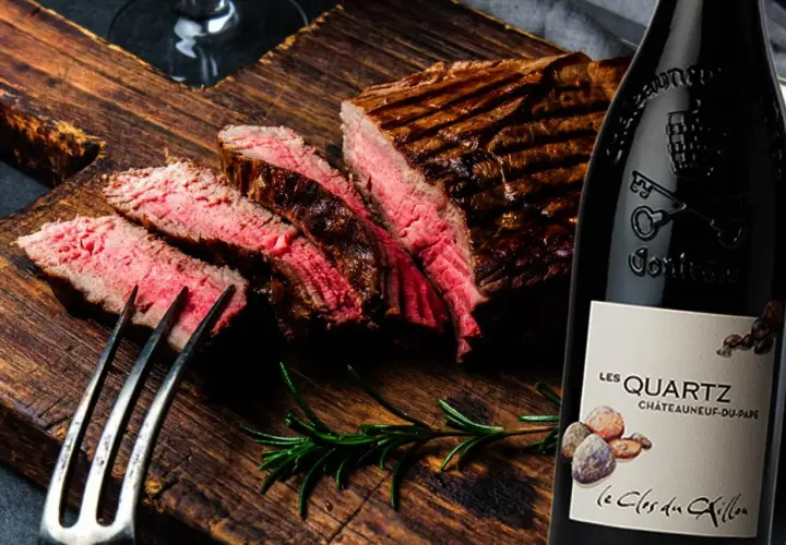 Un steak grillé et tranché sur une planche en bois, accompagné d'une bouteille de vin rouge passe partout.