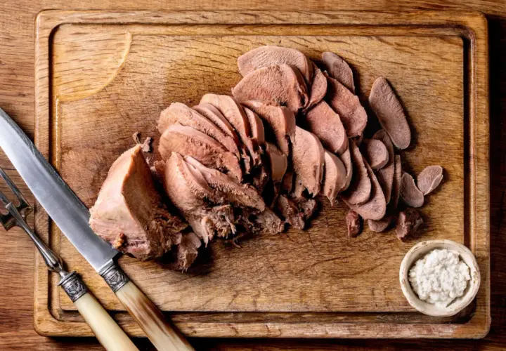 Tranché, la langue de bœuf attend d'être dégustée avec une sauce piquante et des cornichons. Un couteau et une fourchette sont prêts.
