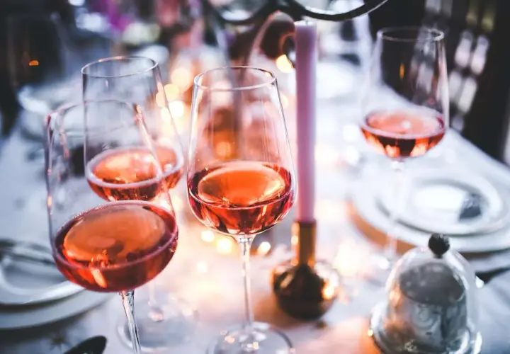 Verres remplis de bon vin rose, prêts pour une célébration festive avec des bougies et des lumières douces.