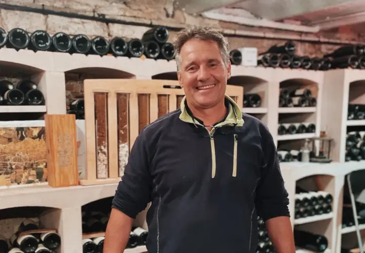 Bruno Clavelier, vigneron souriant, pose dans sa cave remplie de bouteilles.