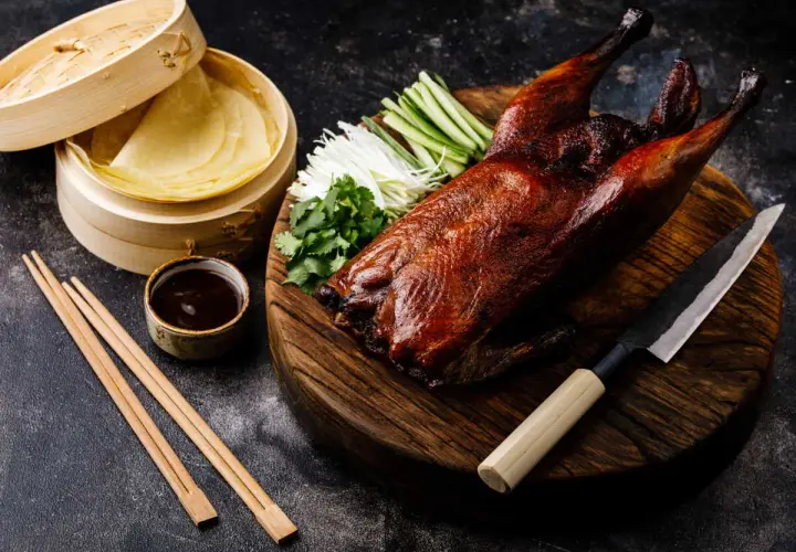 Un canard laqué prêt à être dégusté, accompagné de ses crêpes, sauce, légumes croquants et coriandre. Une recette parfaite pour un repas festif.