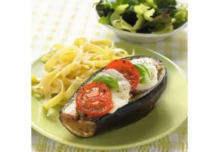 Aubergine farcie de mozzarella, tomates et basilic, servie avec des pâtes et une salade verte. Un plat savoureux et coloré.