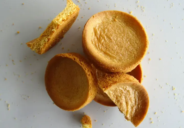 Des biscuits sablés bretons éparpillés, certains entiers, d'autres brisés, sur un fond clair.