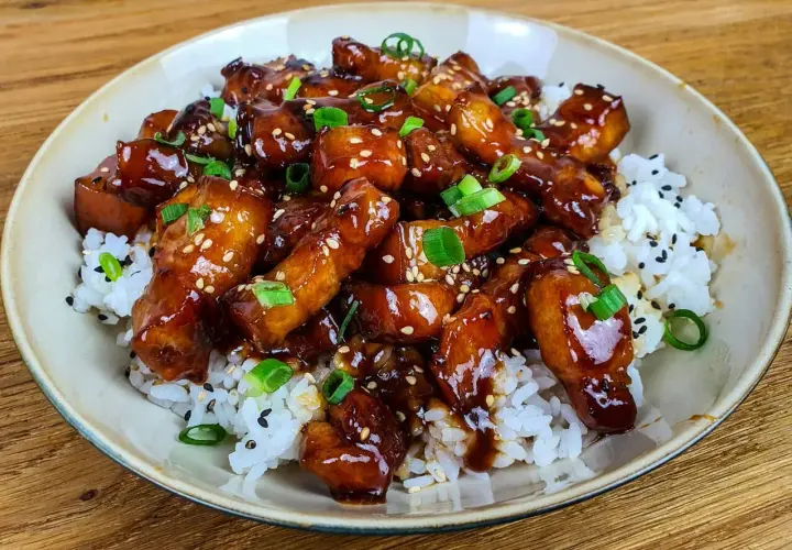 Un plat appétissant de porc au caramel asiatique, garni de graines de sésame et d'oignons verts, servi sur du riz blanc. Une recette à essayer !
