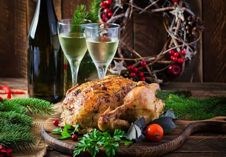 Un chapon rôti, prêt à être dégusté, avec deux verres de vin blanc et une décoration festive. Quel vin avec du chapon pour ce repas de fête ?