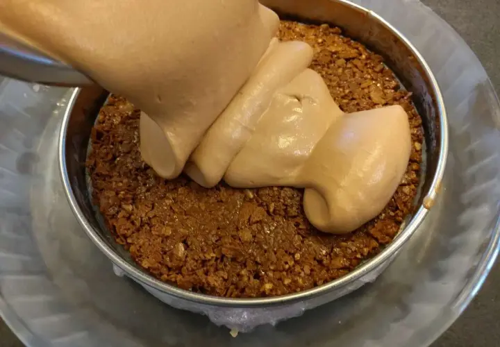 Une crème onctueuse est versée sur une base croustillante praliné feuilletine dans un cercle à pâtisserie.