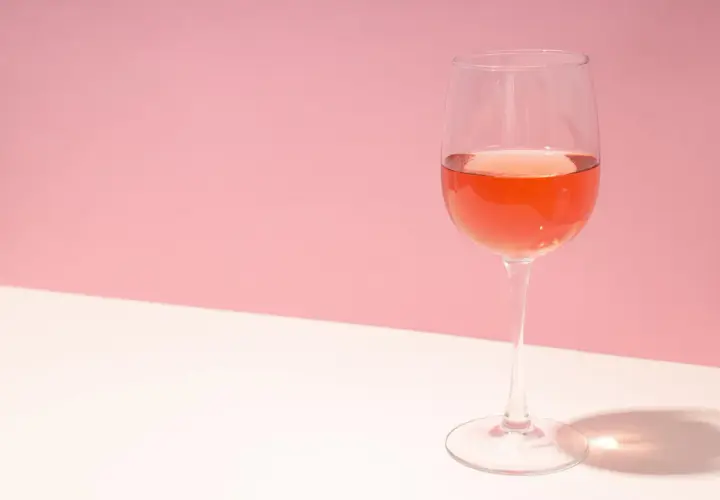 Un verre de rosé de macération, d'une belle couleur orangée, sur un fond rose et blanc.