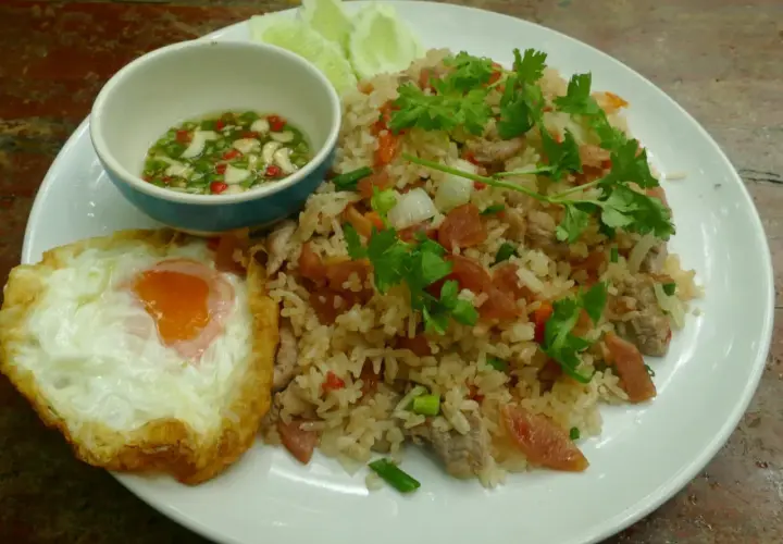 Un plat de riz thaï savoureux avec un œuf au plat, des tranches de concombre et une sauce piquante.