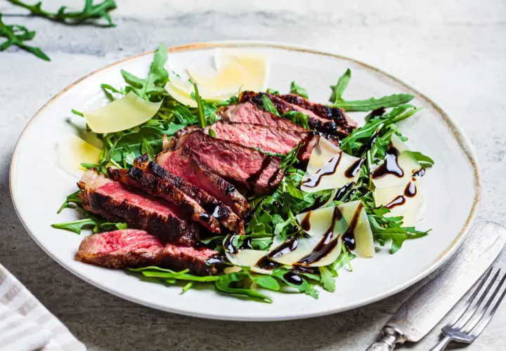 Une assiette de tagliata de boeuf, roquette, copeaux de parmesan et filet de vinaigre balsamique.