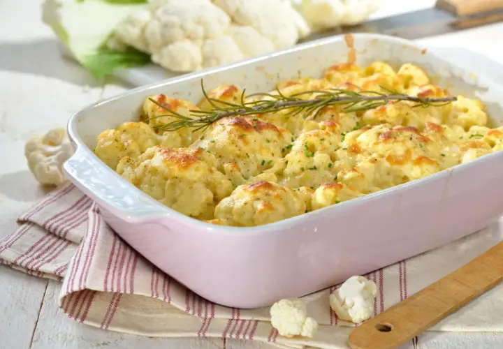 Un plat de gratin de chou-fleur doré et gratiné, garni de romarin frais, prêt à être dégusté.