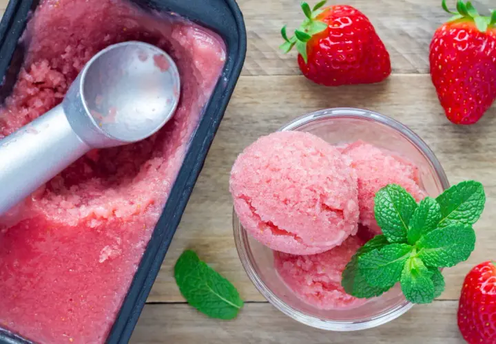 Un délicieux parfait glacé à la fraise, servi dans un bol avec des feuilles de menthe fraîche et des fraises entières.