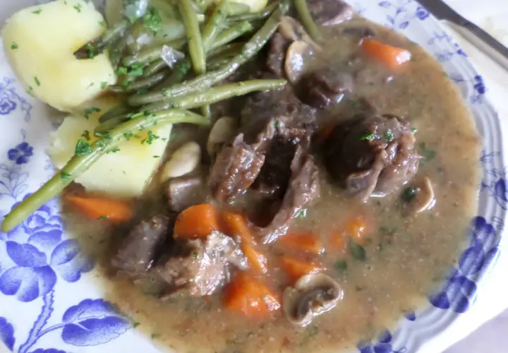Un plat de civet de daim, avec des morceaux de viande tendres, des carottes, des champignons et des haricots verts, accompagné de pommes de terre.