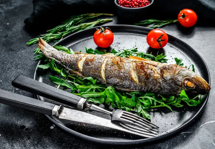 Bar au barbecue, entier et doré, servi sur un lit de roquette avec des tomates cerises et des herbes. Un délice à savourer !