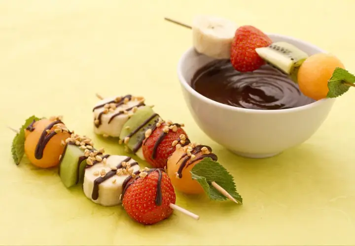 Délicieuses brochettes de fruits, bananes, fraises, kiwis et melons, arrosées de chocolat et de noix, prêtes à être trempées.