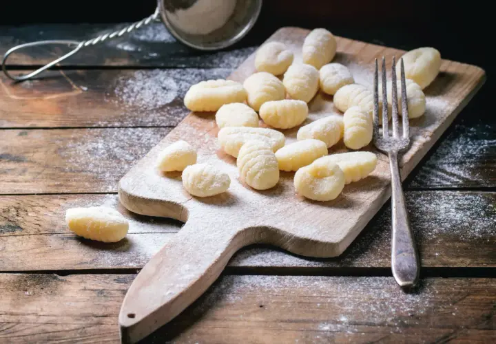 Gnocchis faits maison, prêts pour la cuisson. Une fourchette et une passoire à farine sur une planche en bois saupoudrée de farine, parfaits pour une recette de gnocchi.