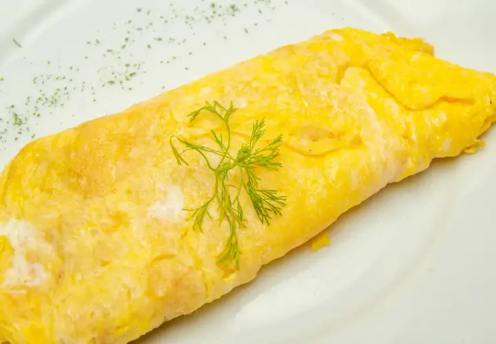 Une omelette au thon, dorée et moelleuse, garnie d'aneth frais sur une assiette blanche. Un délice simple et savoureux.