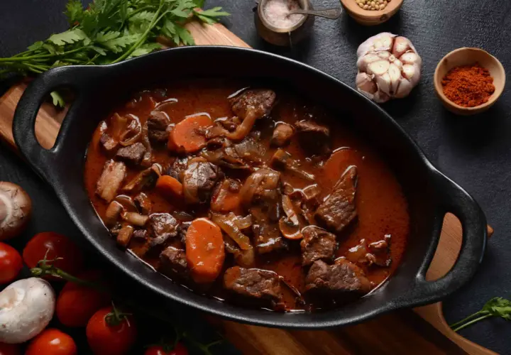 Un plat mijoté de bœuf bourguignon traditionnel, avec des carottes, des oignons et des champignons, prêt à être dégusté.