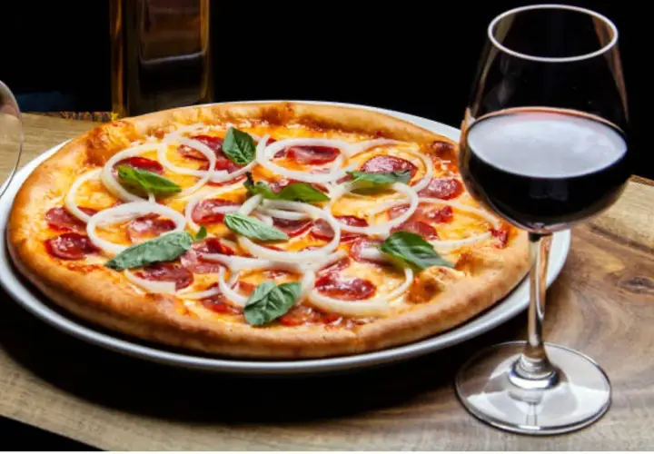 Une pizza garnie d'oignons et de pepperoni, accompagnée d'un verre de vin rouge. La question est : quel vin avec pizza ?