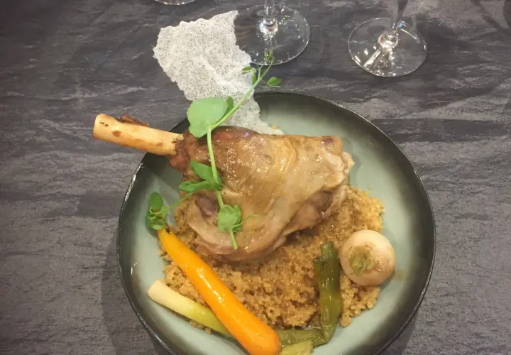 Souris d'agneau braisée au vin, servie sur un lit de couscous avec carottes et navets. Un plat savoureux et réconfortant.