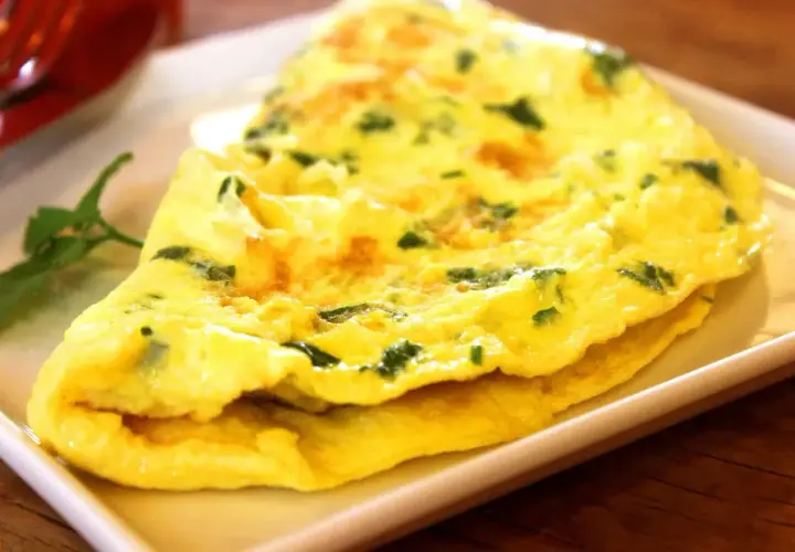 Une omelette au fromage, dorée et moelleuse, parsemée d'herbes fraîches, servie sur une assiette blanche.