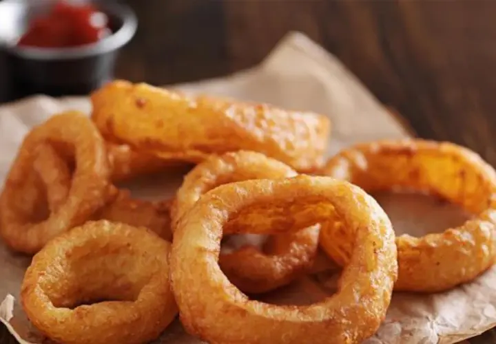Un tas d'oignon rings dorés et croustillants, servis sur du papier brun, avec un petit bol de ketchup en arrière-plan.