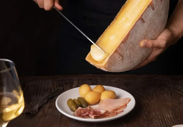 Un verre de vin blanc, parfait pour accompagner la raclette. Sur l'assiette, pommes de terre, cornichons et charcuterie.