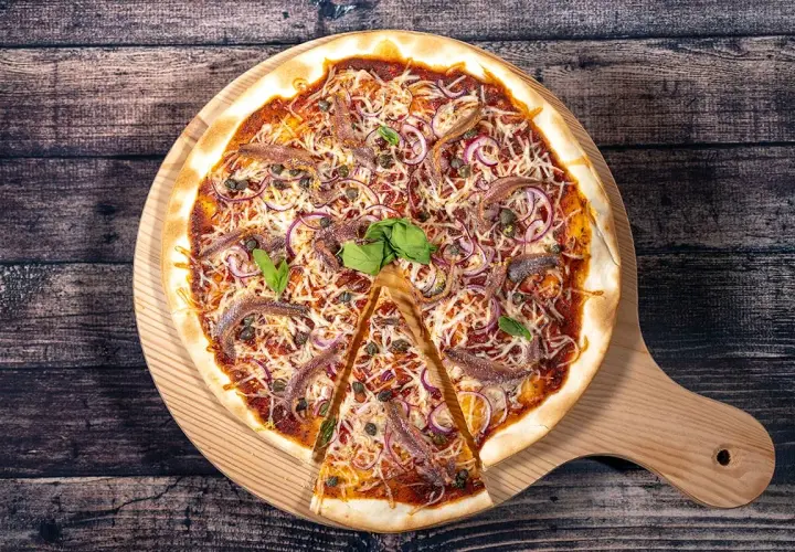 Une pizza savoureuse aux anchois, oignons rouges et câpres, garnie de fromage râpé et de basilic frais, prête à être dégustée.