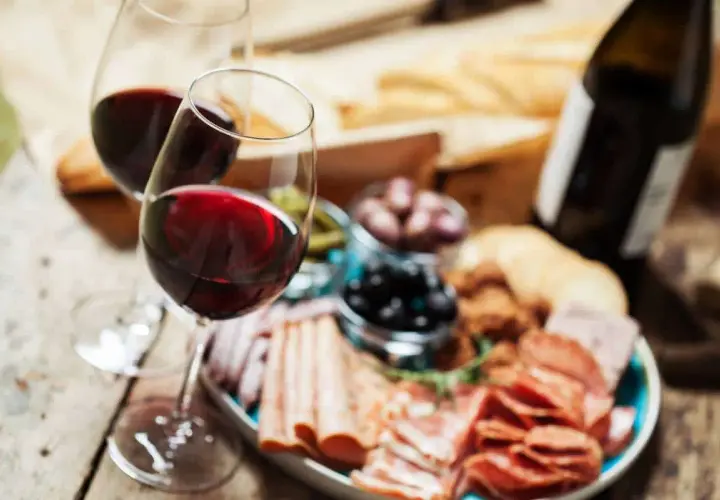 Deux verres de vin rouge, une bouteille, une assiette de charcuterie variée, olives et cornichons. Parfait pour savoir quel vin avec charcuterie.