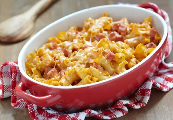 Un plat de gratin de pâtes au jambon, doré et gratiné, servi dans un plat rouge sur une serviette à carreaux.