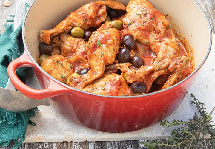 Un plat mijoté de lapin aux olives, baignant dans une sauce tomate savoureuse, garni de thym frais.
