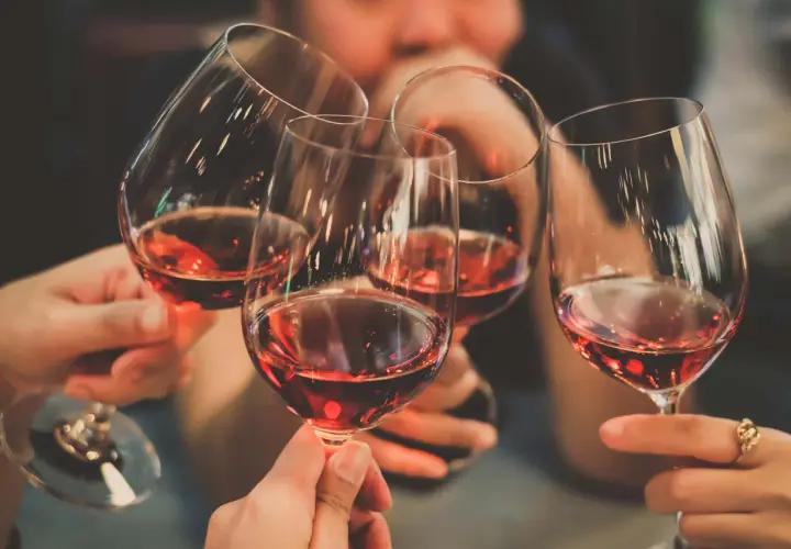 Des mains portent des verres de vin rouge, évoquant la convivialité et les riches régions viticoles de France.