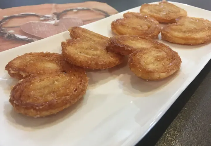 Une assiette blanche présente plusieurs palmiers croustillants, parfaits pour une recette facile.