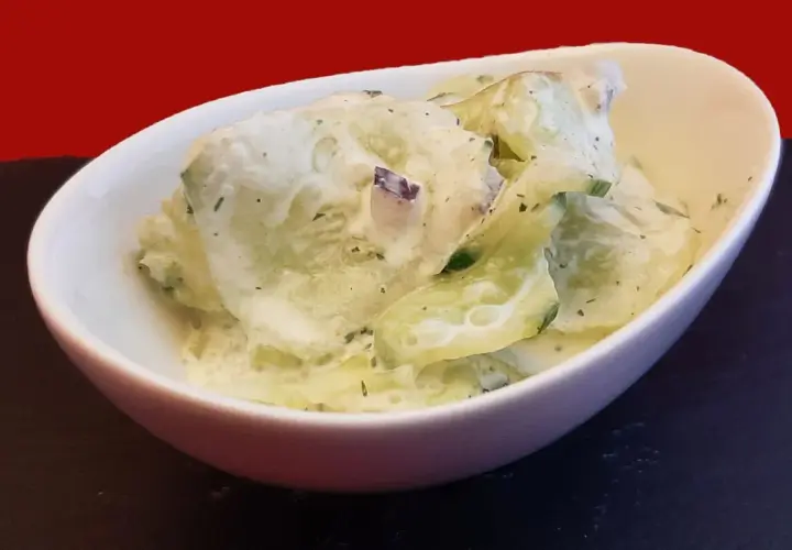 Un bol de concombre à la crème, garni d'herbes fraîches, prêt à être dégusté.
