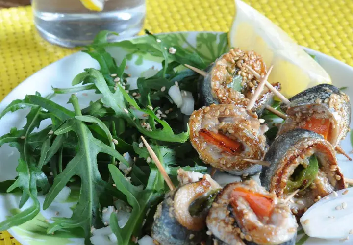 Rouleaux de sardines à la plancha, enrobés de sésame, servis avec une salade verte et un quartier de citron.