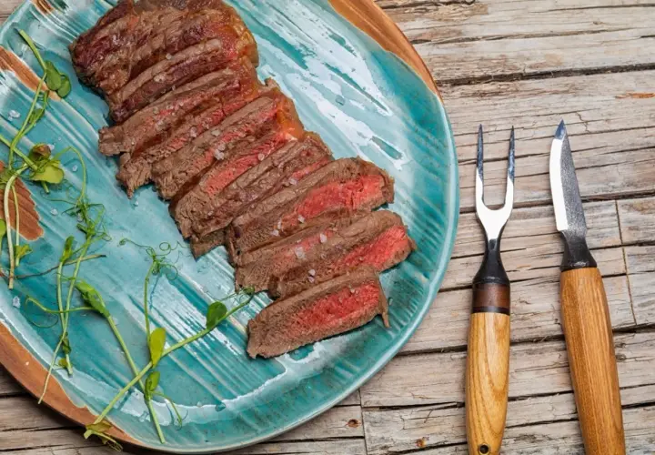 Tranches d'onglet de bœuf saignant, parsemées de gros sel, sur une assiette turquoise. Une recette simple pour un plat savoureux.