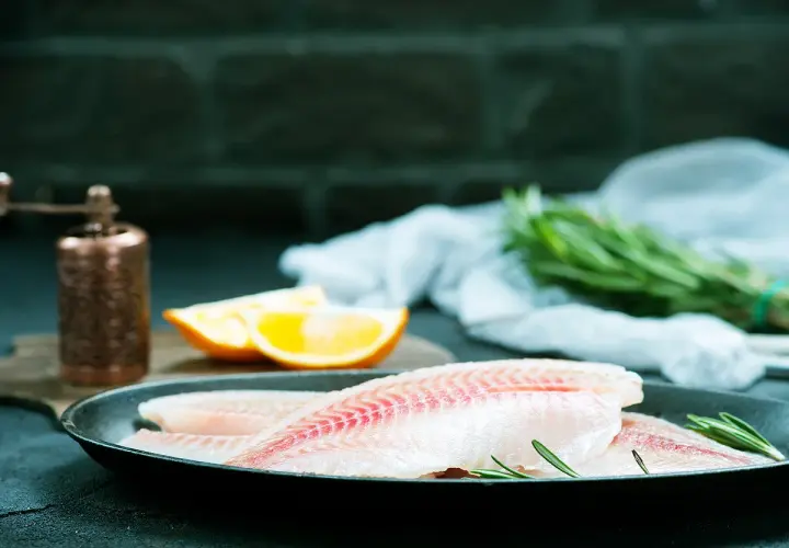 Filets de poisson crus dans une poêle, prêts pour un maquereau au vin blanc. Oranges et romarin à proximité.