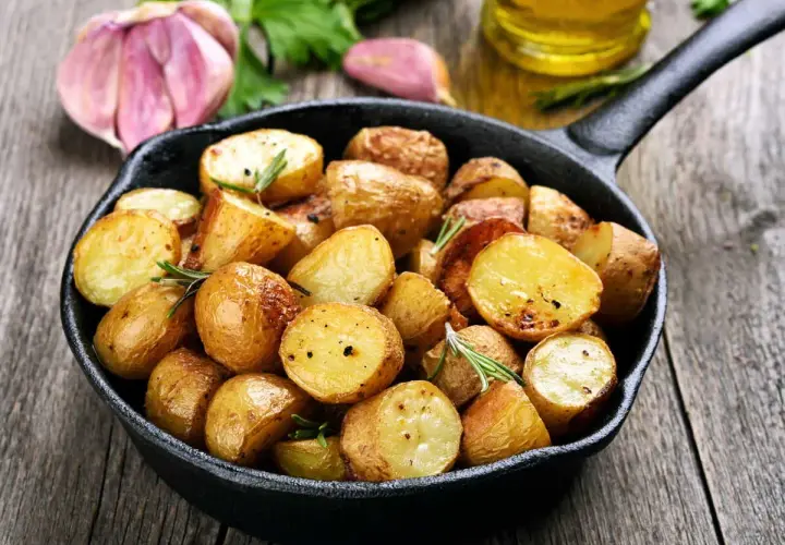 Poêlée de pommes de terre sautées dorées et croustillantes, garnies de romarin frais, avec de l'ail et de l'huile d'olive en arrière-plan.
