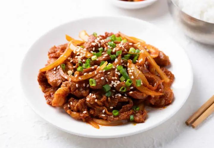 Délicieux boeuf aux oignons, garni de graines de sésame et de ciboule, servi sur une assiette blanche.