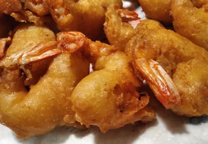 Gros plan sur des beignets de crevette dorés et croustillants, prêts à être dégustés. Les queues des crevettes dépassent de la pâte.