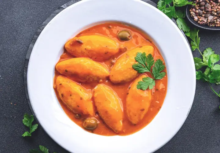 Assiette de quenelles de brochet en sauce tomate, garnie de persil et d'olives.